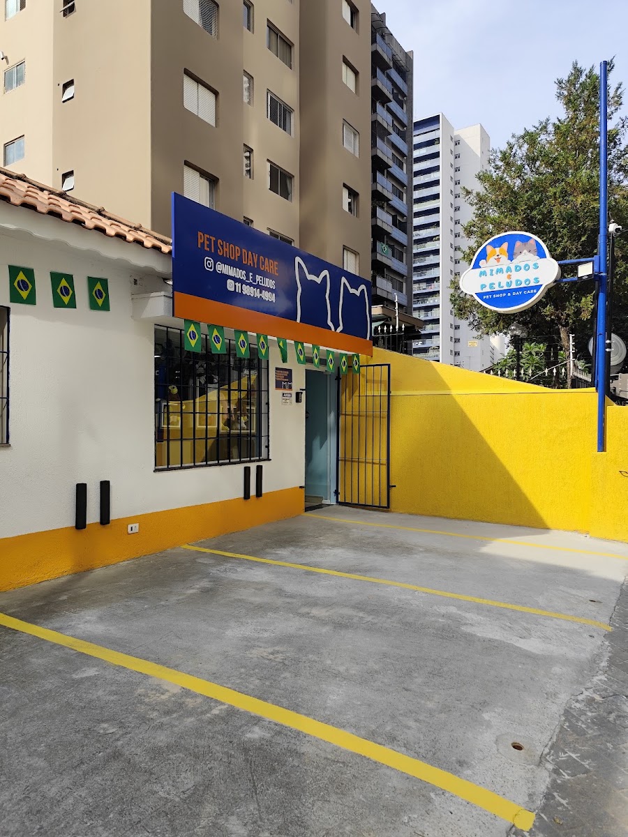 Fachada do Mimados e Peludos Pet Shop & Day Care, com placa azul, muro amarelo e bandeirinhas do Brasil